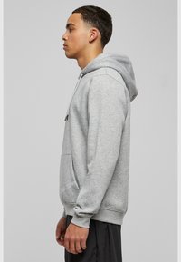 Grijze katoenen hoodie met een kangoeroezak, trekkoordkap, ribgebreide manchetten en zoom. Soepele textuur en casual pasvorm. Zijaanzicht weergegeven.