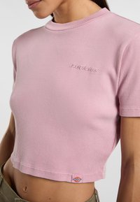 Růžový žebrovaný crop top s krátkými rukávy, který má na hrudi vyšívané logo a značkovou visačku na lemu.