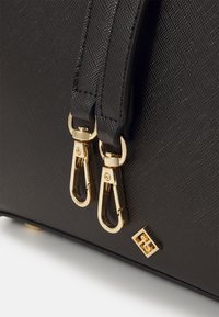 Sort tekstureret håndtaske med guldhardware, to lynlåse og logoaccent. Materialet præsenterer en fin, holdbar finish.