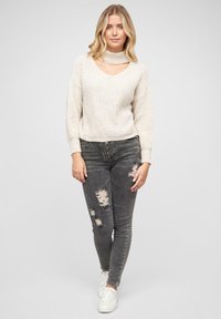 Beige knitted sweater with a scooped neckline and high collar, paired with grey ripped skinny jeans and white sneakers.