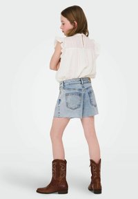 Blusa a righe rosa chiaro con maniche arricciate, pantaloni corti in denim blu con bordi sfrangiati e stivali cowboy marroni con cuciture decorative.