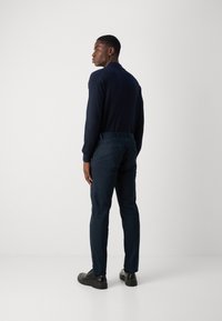 Marineblauw overhemd met lange mouwen en donkerblauwe broek, met een slank ontwerp. Glad materiaal met een getailleerde pasvorm, gecombineerd met zwarte schoenen.