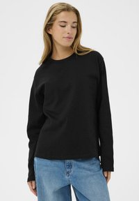 Czarna longsleeve w bawełnie, z okrągłym dekoltem i luźnym krojem. Połączona z jasnoniebieskimi dżinsami dla casualowego wyglądu.