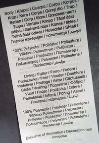 Etichetta di cura con testo multilingue che dettagli la composizione dei materiali: 100% poliestere, informazioni sull'imbottitura e istruzioni per la manutenzione.