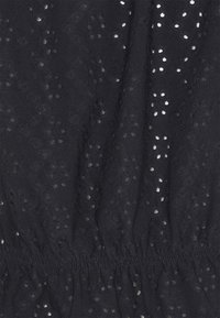 Svart tyg med en texturerad mönster som har små utskurna hål arrangerade i en diamantformation; detaljer med elastisk midja.