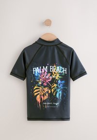 Maglia da surf nera a maniche corte con stampe di foglie tropicali colorate e la scritta "Palm Beach, Florida" sul retro. Tessuto liscio ed elastico.