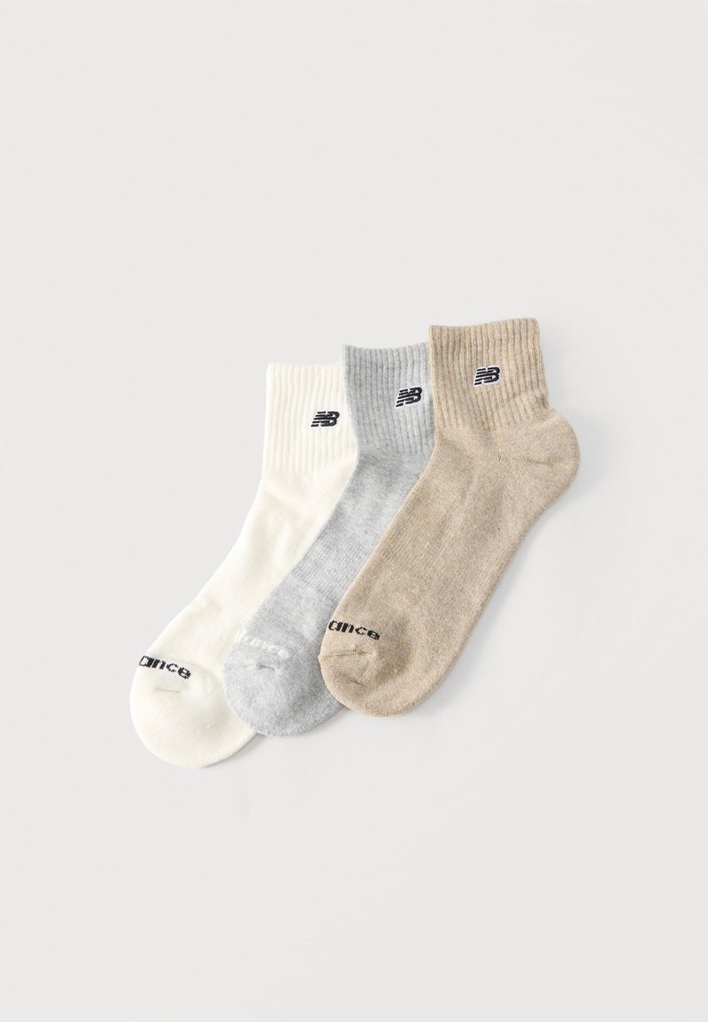 Trois paires de chaussettes à côtes, blanches, gris clair et beige, chacune avec un logo New Balance noir sur la bande et le texte "Balance" sur l'orteil.