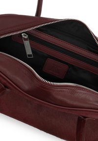 Burgundy leather handbag with smooth texture, zip closure, and a black fabric interior. Features an internal zip pocket and logo accent.