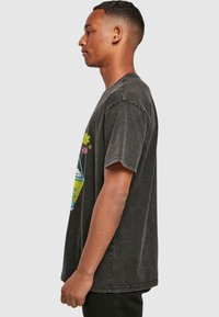 Camiseta de algodón negra con un corte relajado, mangas cortas y un diseño gráfico colorido que presenta flores y formas geométricas en la parte frontal.