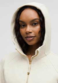 Svijetlosmeđa dukserica sa zatvaračem, s kapuljačom, ima zlatni zatvarač, teksturiranu tkaninu i šavnu obradu na ramenima.