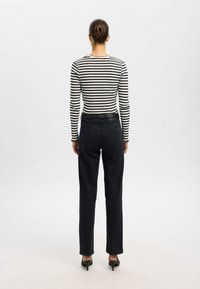 Sorte høye liv jeans kombinert med en svart og hvit stripete langermet topp, som har en tettsittende design og minimale detaljer.