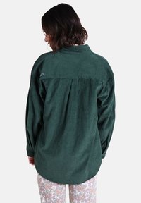 Chemise en velours côtelé vert à manches longues avec détail de pli au dos ; présente un logo discret sur l'épaule gauche et une coupe décontractée.