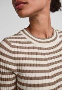 Zbliżenie na osobę ubraną w beżowy i biały sweter w poziome paski z prążkowanej tkaniny i okrągłym dekoltem.