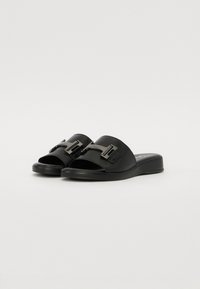 Sorte skinnsandaler med glatt faux skinn overdel, med bred stropp og metallspenne-detaljer. Flat såle, enkel design.