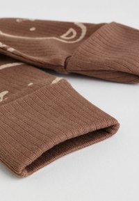 Mangas de punto acanalado marrón con un diseño estampado, mostradas dobladas y extendidas sobre una superficie clara.