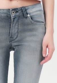 Jeans de mezclilla gris deslavado con un corte ajustado, que cuentan con una cremallera, bolsillos frontales y detalles de costura sutiles en la cinturilla.