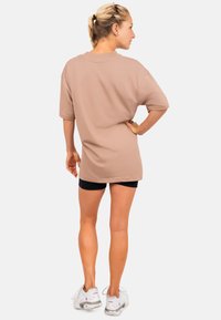 Lichtbruine oversized t-shirt met korte mouwen, gemaakt van katoen, ronde halslijn, gedragen met zwarte shorts, gecombineerd met witte sportschoenen.