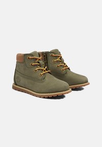 Stivaletti alla caviglia in suede verde con accenti in pelle marrone, lacci gialli, zip laterale e suola in gomma testurizzata. Presenta un logo sul lato.