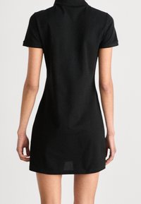 Svart klänning med krage, kort ärm, figursydd design och något texturerad tyg. Knälång med rak skärning och inga synliga mönster.