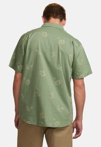 Camicetta verde a maniche corte con motivo a palme in una tonalità più chiara. Realizzata in tessuto leggero con una vestibilità comoda e orlo dritto.
