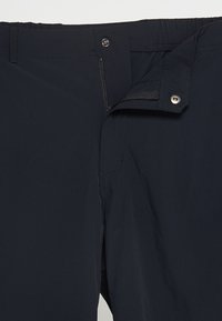 Granatowe spodnie o gładkiej fakturze, z zamkiem błyskawicznym i zapięciem na guzik, elastycznym paskiem w talii oraz subtelnymi detalami przeszycia.