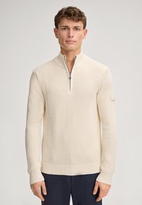 Pullover in maglia beige chiaro con trama, collo con zip e polsini a coste. Presenta un piccolo emblema sulla manica sinistra. Tessuto morbido, vestibilità regolare.
