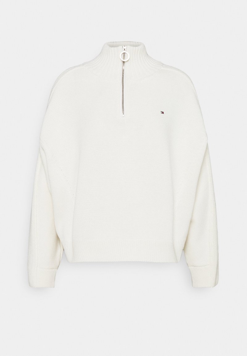Weißer gestrickter Pullover mit hohem Kragen, halbem Reißverschluss vorne und gerippten Bündchen. Bewusst hat er ein kleines Logo auf der linken Brustseite.