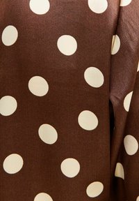 Bruine stof met grote crèmekleurige stippen; gladde textuur; het materiaal lijkt lichtgewicht. De stippen variëren in grootte en zijn regelmatig verdeeld.