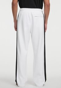 Weiße Jogginghosen mit schwarzen Seitenstreifen, elastischem Bund und Gesäßtasche. Der Stoff wirkt weich; lockere Passform mit geradem Bein design.
