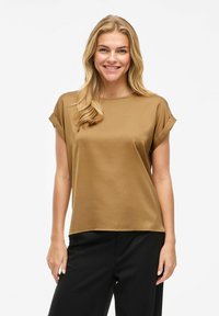 Haut en satin marron avec des manches courtes retroussées, un col rond et une coupe décontractée, associé à un pantalon noir. Texture lisse, détails minimalistes.