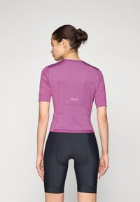 Maillot de cyclisme à manches courtes en mauve avec une coupe ajustée, des coutures accentuées et un détail de logo au dos, associé à un short de cyclisme noir.