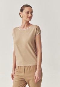 Top beige a maniche corte con scollatura rotonda e dettagli a contrasto bianchi, realizzato in un tessuto liscio e leggero. Abbinato a pantaloni coordinati.