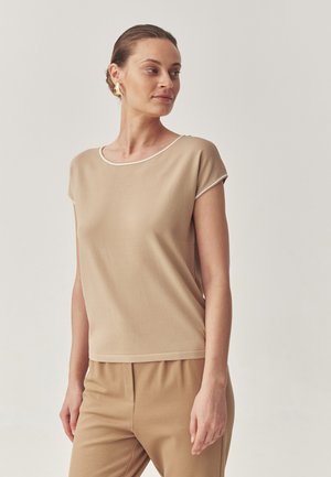 Top beige a maniche corte con scollatura rotonda e dettagli a contrasto bianchi, realizzato in un tessuto liscio e leggero. Abbinato a pantaloni coordinati.