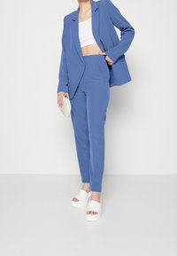 Ljusblå skräddarsydd kostym med kavaj och matchande byxor, kombinerad med en vit kort topp och kraftiga vita platåsandaler.