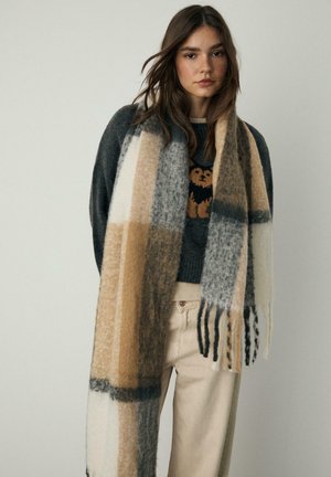 Stribet tørklæde i blødt uldmix, der har farverne beige, grå og hvid. Udsmykket med frynsede ender og en struktureret overflade.