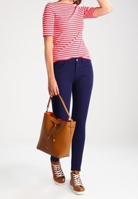 Červené a bílé pruhované tričko s krátkým rukávem, námořnické skinny džíny, hnědá kožená taška ve tvaru kyble a hnědé tenisky s bílými tkaničkami.