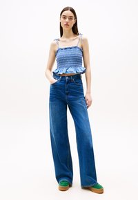 Lyseblå smokkede crop-top med volangkant, kombinert med høyt liv brede bukser i blå denim og grønne plattform-sneakers.