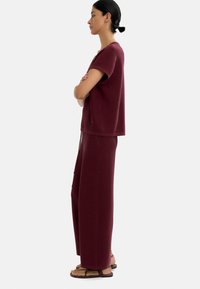 Bordowy dwuczęściowy zestaw składający się z bluzki z krótkim rękawem o pudełkowym kroju oraz spodni z szerokimi nogawkami, wykonany z fakturowanej tkaniny w luźnym kroju.