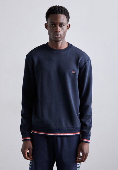 Sudadera azul marino de algodón suave, con cuello redondo acanalado, detalles de rayas rojas y blancas en el dobladillo y los puños, y un pequeño logotipo.