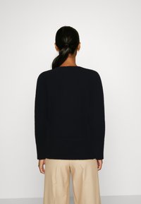 Suéter de punto azul marino con cuello redondo, mangas largas y dobladillo acanalado, combinado con pantalones de pierna ancha beige.