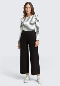Chemise blanche à manches longues avec des rayures noires horizontales, associée à un pantalon large taille haute noir et des baskets blanches. Tenue simple et décontractée.