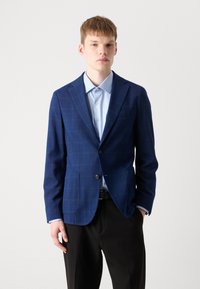 Mornarsko moder blejzer s karirastim vzorcem, dvema sprednjima žepoma, zapiranjem na en gumb in s ovratnikom, v kombinaciji s svetlo modro srajco.