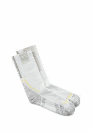 Par de calcetines blancos hasta el tobillo con zonas grises en el talón y la punta, líneas de acento amarillas y patrones grises sutiles sobre un fondo blanco liso.