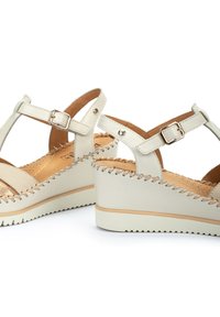 Sandalias de cuña beige con tira al tobillo, parte superior de cuero, detalles cosidos y plantilla en tono marrón. Suela texturizada para agarre y estabilidad.