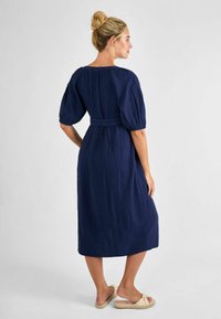Abito blu navy realizzato in tessuto texturizzato, con maniche a sbuffo corte, vita legata e orlo fino alla caviglia, abbinato a sandali chiari.