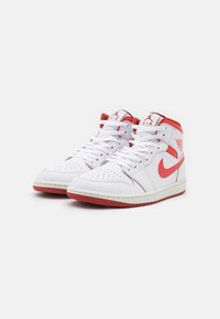 Sneaker alte bianche con accenti rossi e logo Nike, con punta perforata, lacci bianchi e suola in gomma testurizzata.