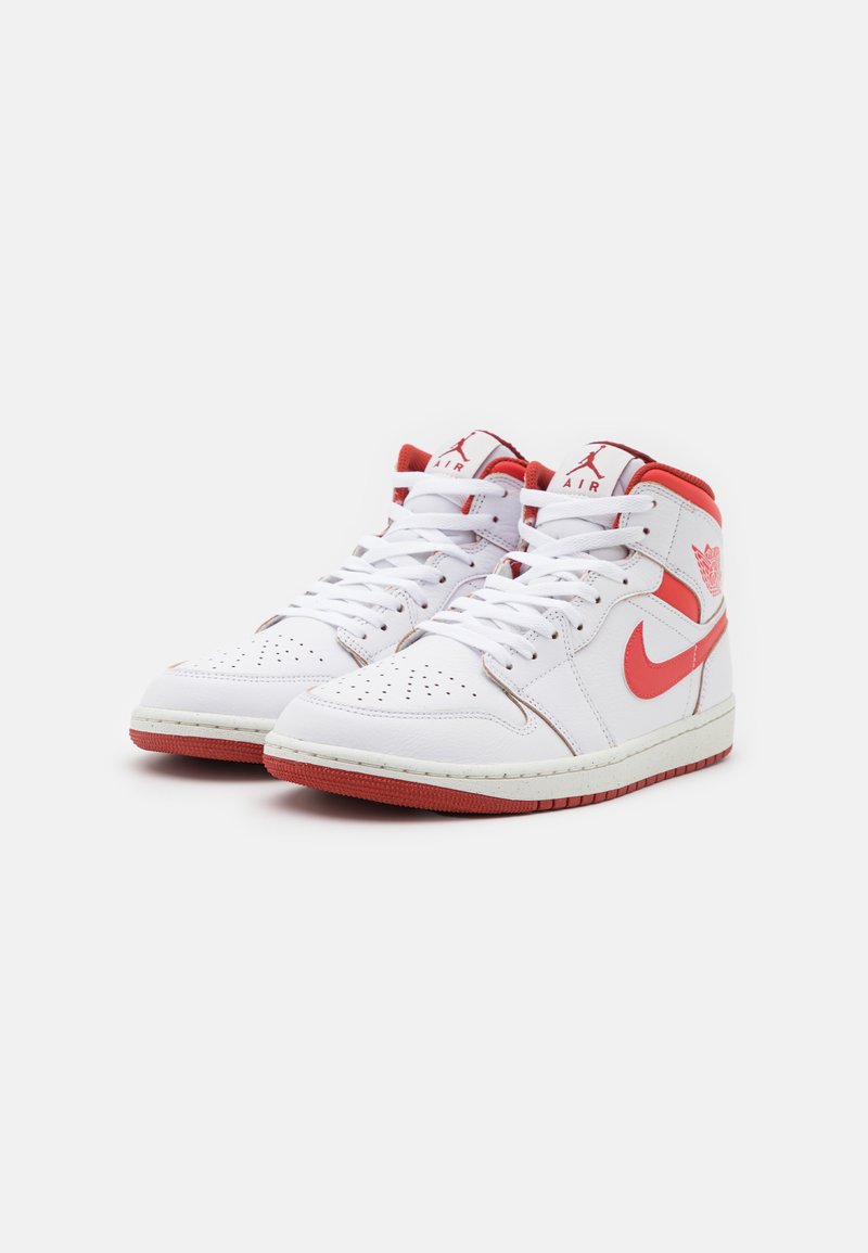 Zapatillas altas blancas con acentos rojos y logo de Nike, que cuentan con una caja de dedos perforada, cordones blancos y suela de goma texturizada.
