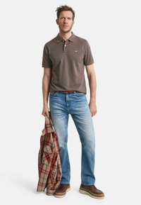 Brun polo-tröja med korta ärmar, ljusblå jeans och bruna stövlar. Håller en röd och grå rutig flanelljacka. Enkelt mönster och texturer.