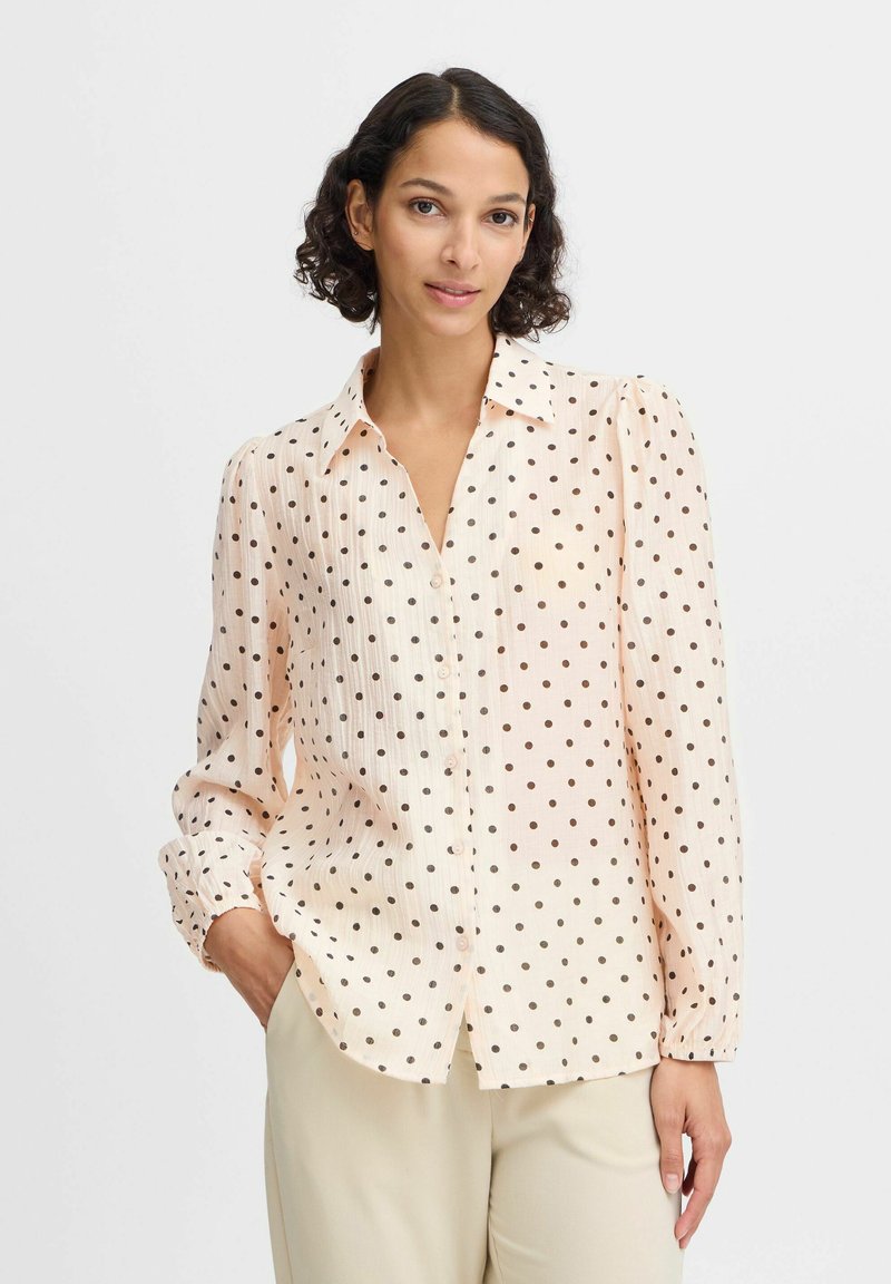 Cream blouse with black polka dots, button-down front, long sleeves with button cuffs, lightweight textured fabric, and a relaxed fit.