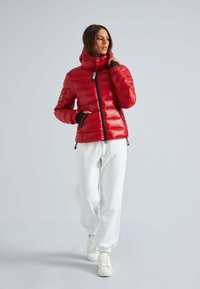 Rode pufferjas met een hoge kraag, zwarte accenten, ritszakken en een snug fit, gedragen met witte sweatpants en witte sneakers.